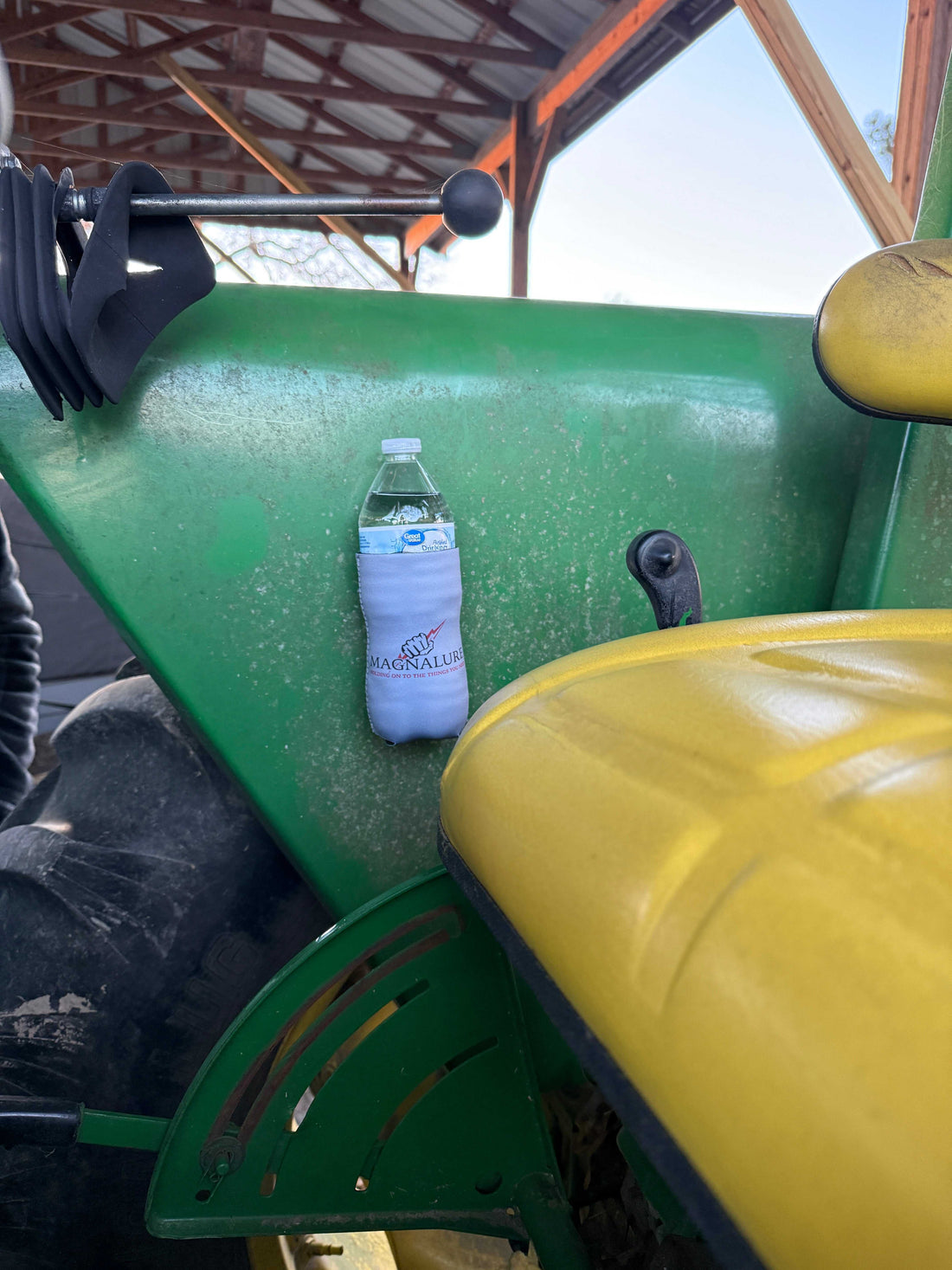 Magnetic koozie holding a bottle on a green tractor for hands-free beverage convenience outdoors