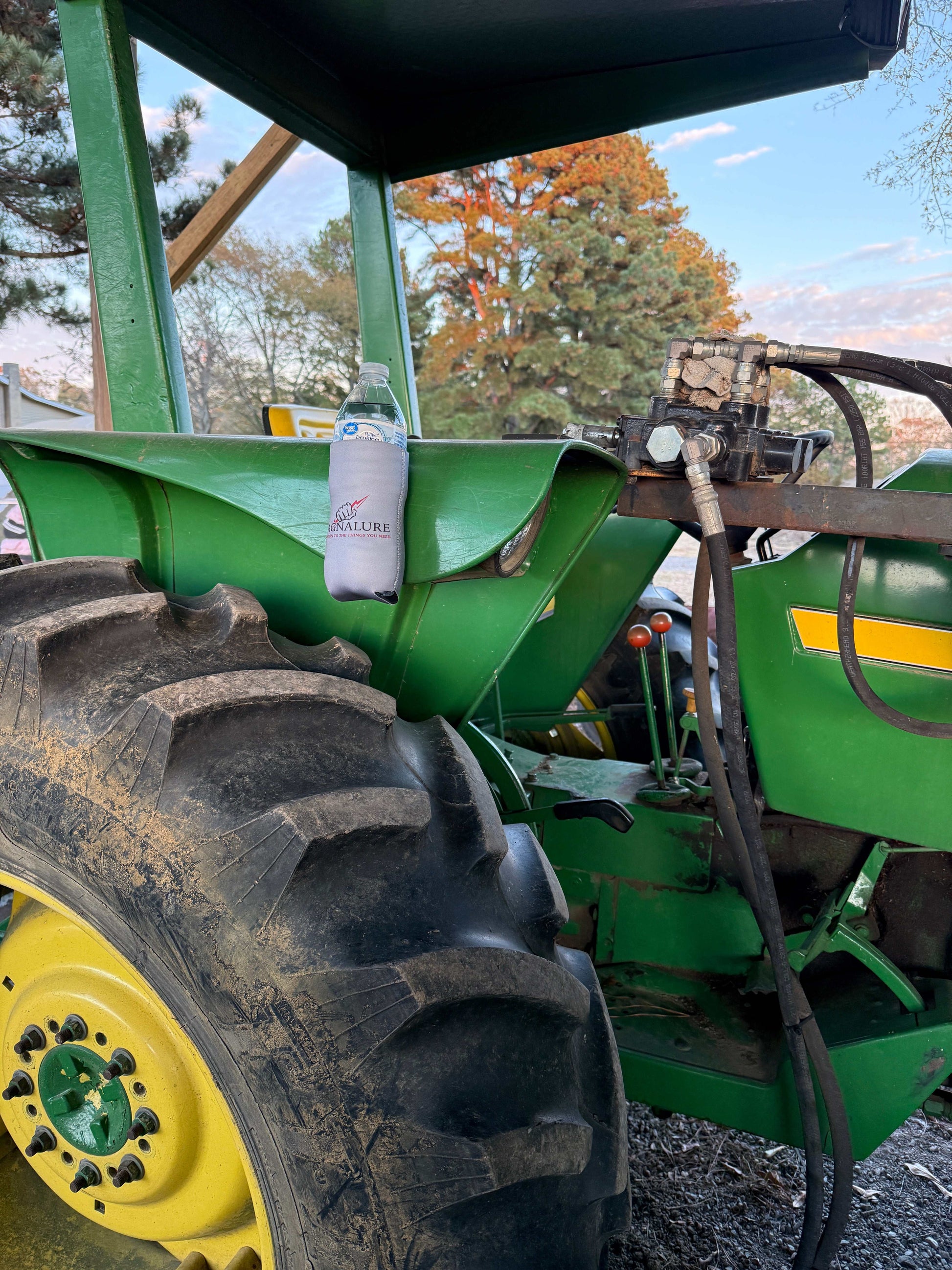Magnetic koozie holding a bottle on a green tractor for hands-free beverage convenience outdoors